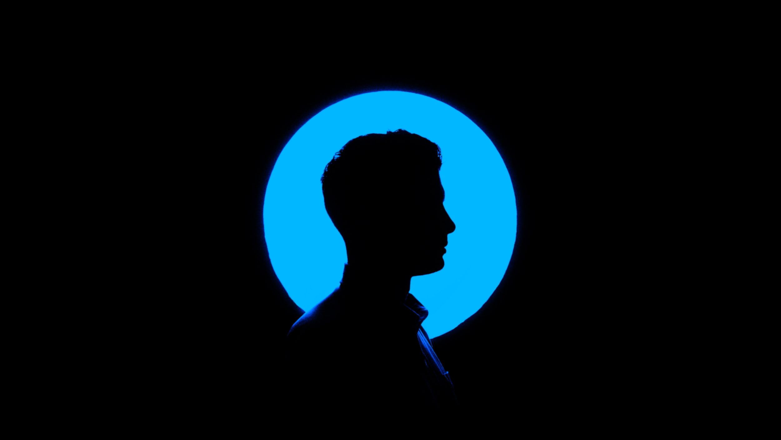 Silhouette of a man in front of a blue circular light.