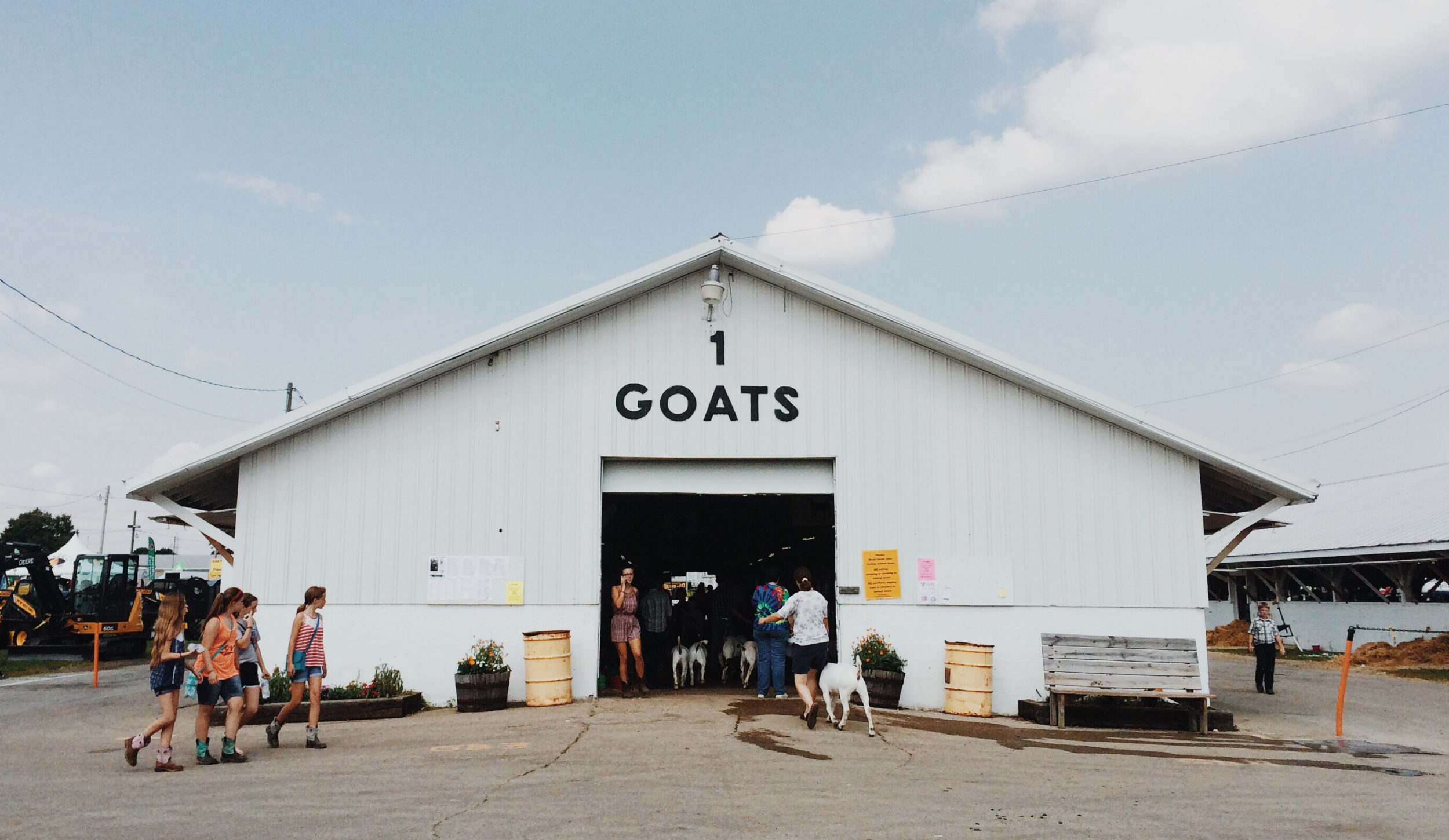 People and goats entering a white building that says, "1 GOATS" on it