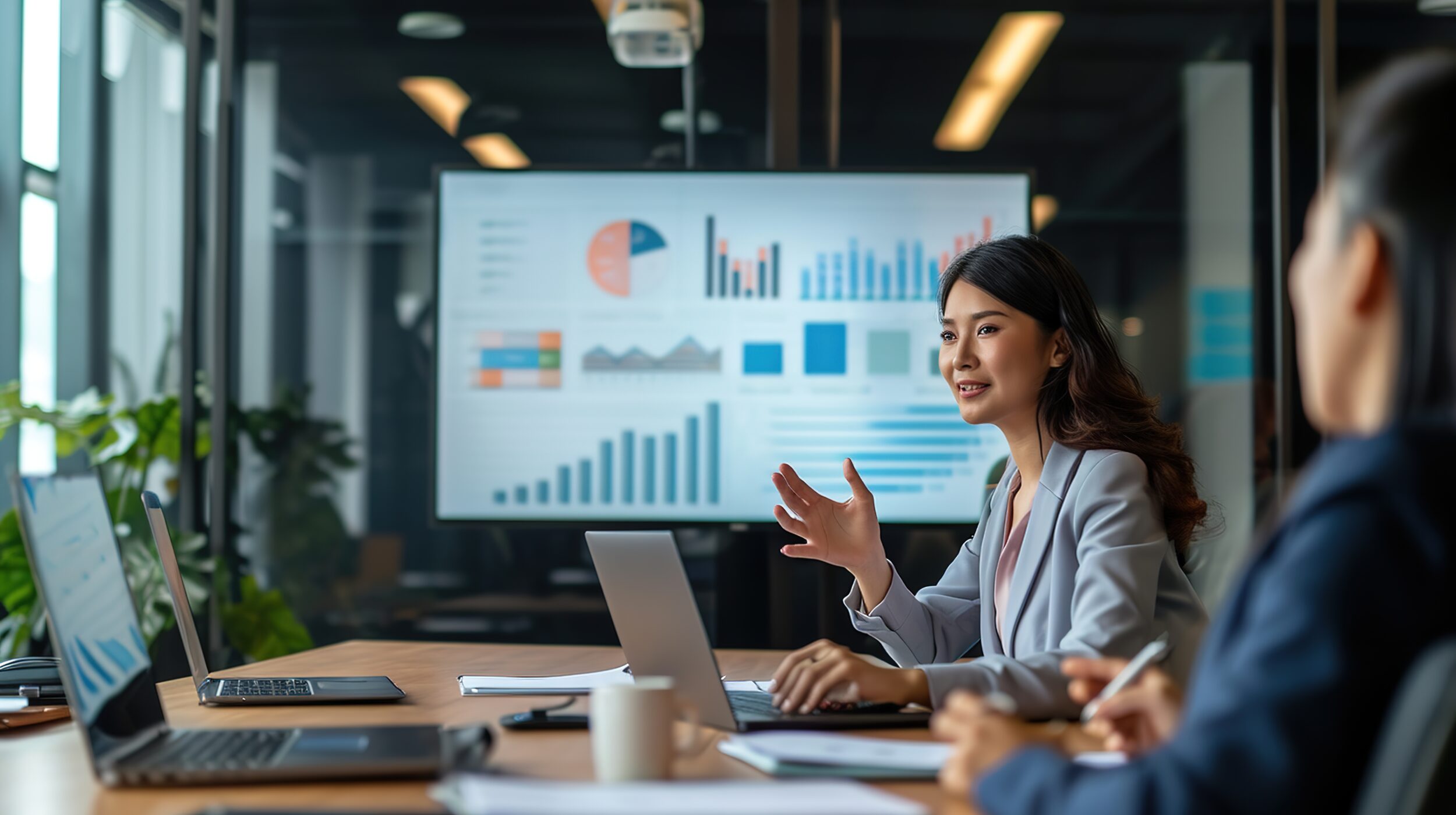 Young businesswoman presenting data analysis dashboard on TV screen in modern meeting. Business presentation with group of business people in conference room