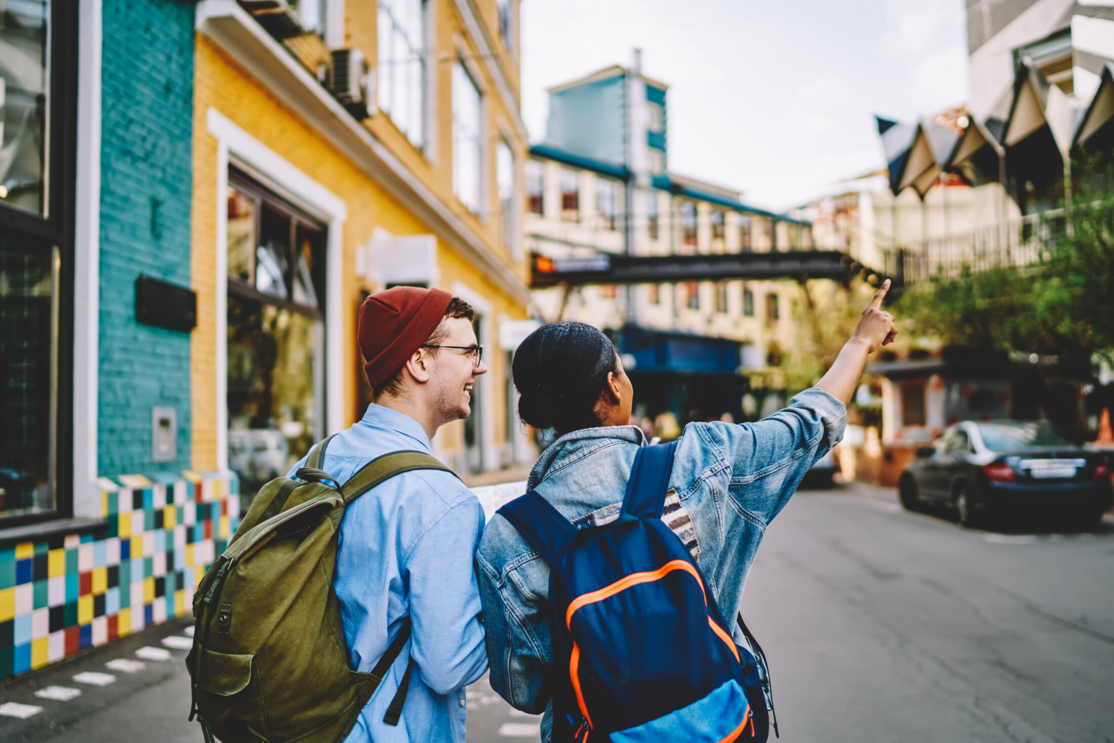 Back view of male and female backpackers enjoying live communication during travel experience for exploring city, happy hipster guys talking while walking at touristic urban setting during vacations